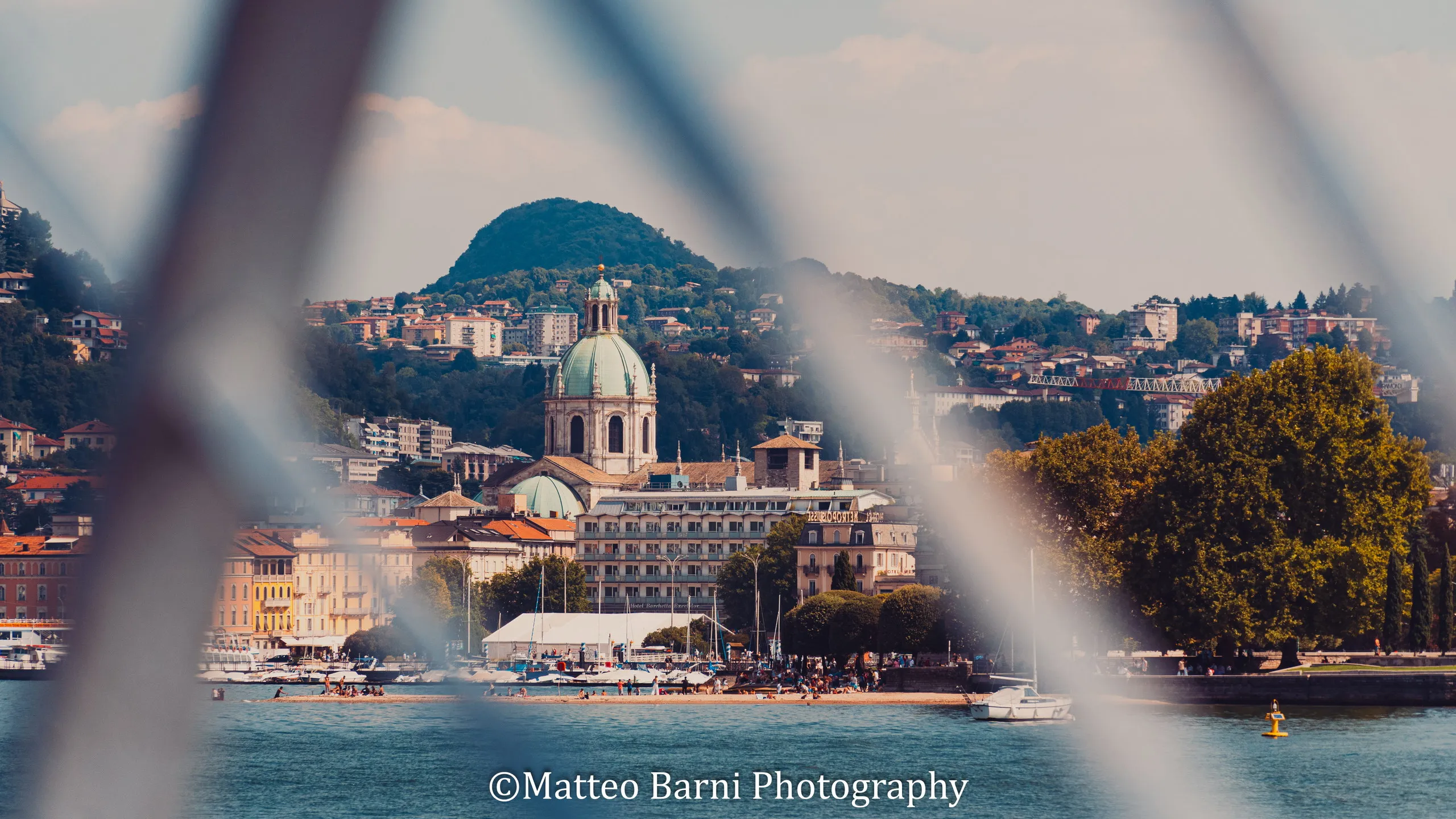 Una città sul lago con una grande cupola e la collina alle spalle, vista attraverso le sbarre sfocate di una ringhiera